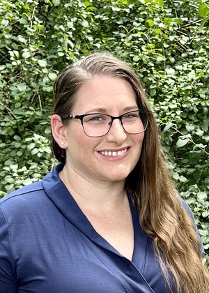 A headshot of Jackie Wolf standing in front of a hedge.