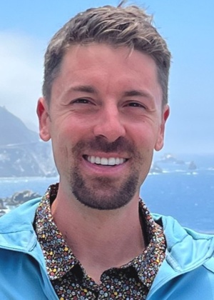 A headshot of Michael Clark. There are cliffs and a body of water in the background.