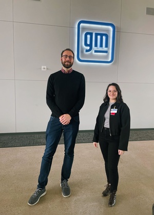 An image of Ian Geiman and Samantha Brown posing in front of a blue, illuminated "gm" sign