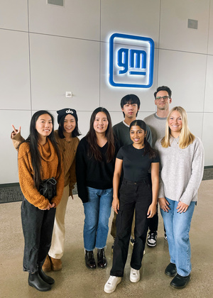An image of a small group of students posing in front of a blue, illuminated "GM" sign