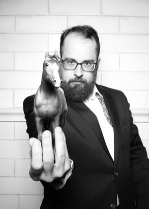 A black and white headshot of José-Antonio Rubio holding a toy horse out toward the camera