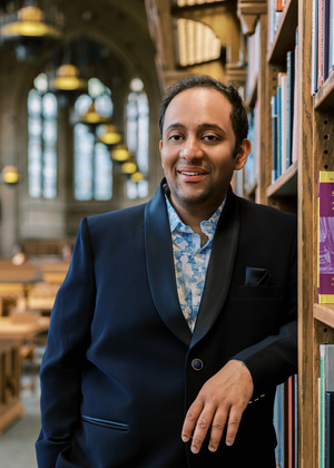A headshot of Venkatesh Potluri leaning against a bookshelf in a library.