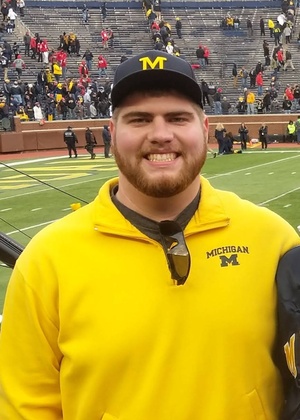 Josh Geschke wearing a University of Michigan shirt and baseball hat in a stadium.