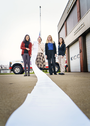 Four students hold a long paper in front of a fire station