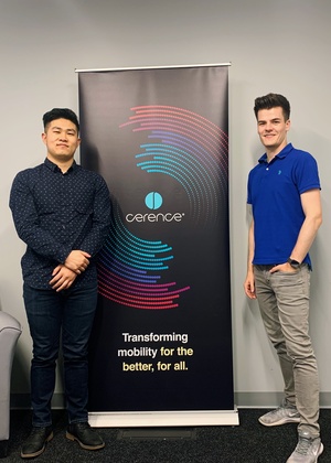 Percy Long stands with his internship supervisor in front of a Cerence sign.