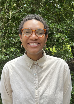 A headshot of Jordan Rhym in front of green hedges