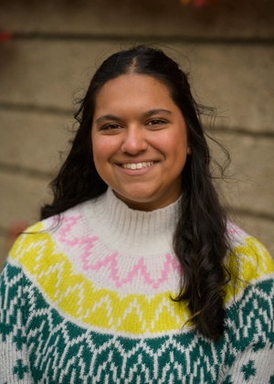 An image of Aayana Anand wearing a brightly patterned sweater with a neutral background.