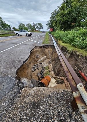 An Ypsilanti township road washout following an August 2023 storm — a large portion of the road has given way, revealing mud and pipes beneath 