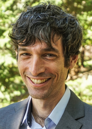 Headshot of Ro'ee Levy, taken outside among foliage on a sunny day. 