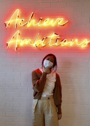 Louise Jaemin Lee standing under a neon sign that says Achieve Ambitions