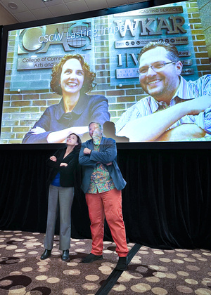 Cliff and Nicole stand in front of a projection screen showing an old photo of them together