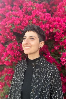 A headshot of Tam Rayan standing in front of a bush full of flowers