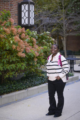 Olga Hamilton poses in front of a flowering autumn bush wearing backpack