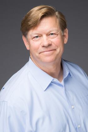 A headshot of John Thompson against a dark gray background
