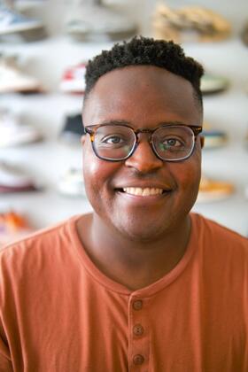 A headshot of Hope Tambala with a display of colorful sneakers, out of focus, behind him