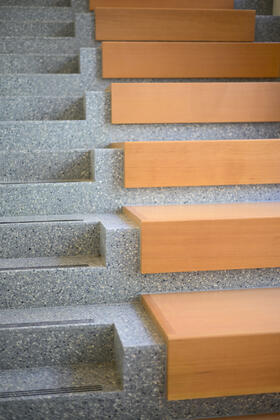A detail shot of a staircase, with gray terrazzo steps on the left and cherry wood embedded benches on the right