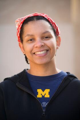An image of Christine Carethers standing on campus, wearing a U-M t-shirt and a red bandana