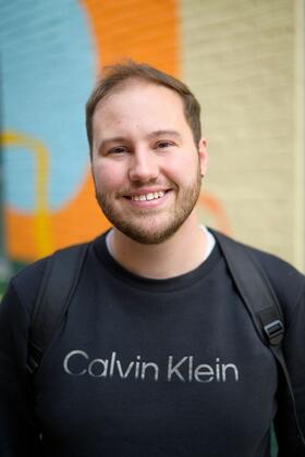 A photo of Joey Quick standing on campus with a mural wall behind him.