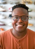 A headshot of Hope Tambala with a display of colorful sneakers, out of focus, behind him