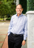 Photo of Dr. David J. Cooper, a man leaning against a stone fence, smiling. 