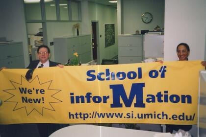 Daniel Atkins and Olivia Frost hold a bright yellow banner that reads "School of Information" and "We're new!"