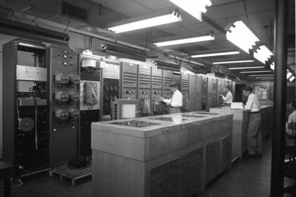A room holding a wall-to-wall computer in 1953, with a couple technicians standing in front of it